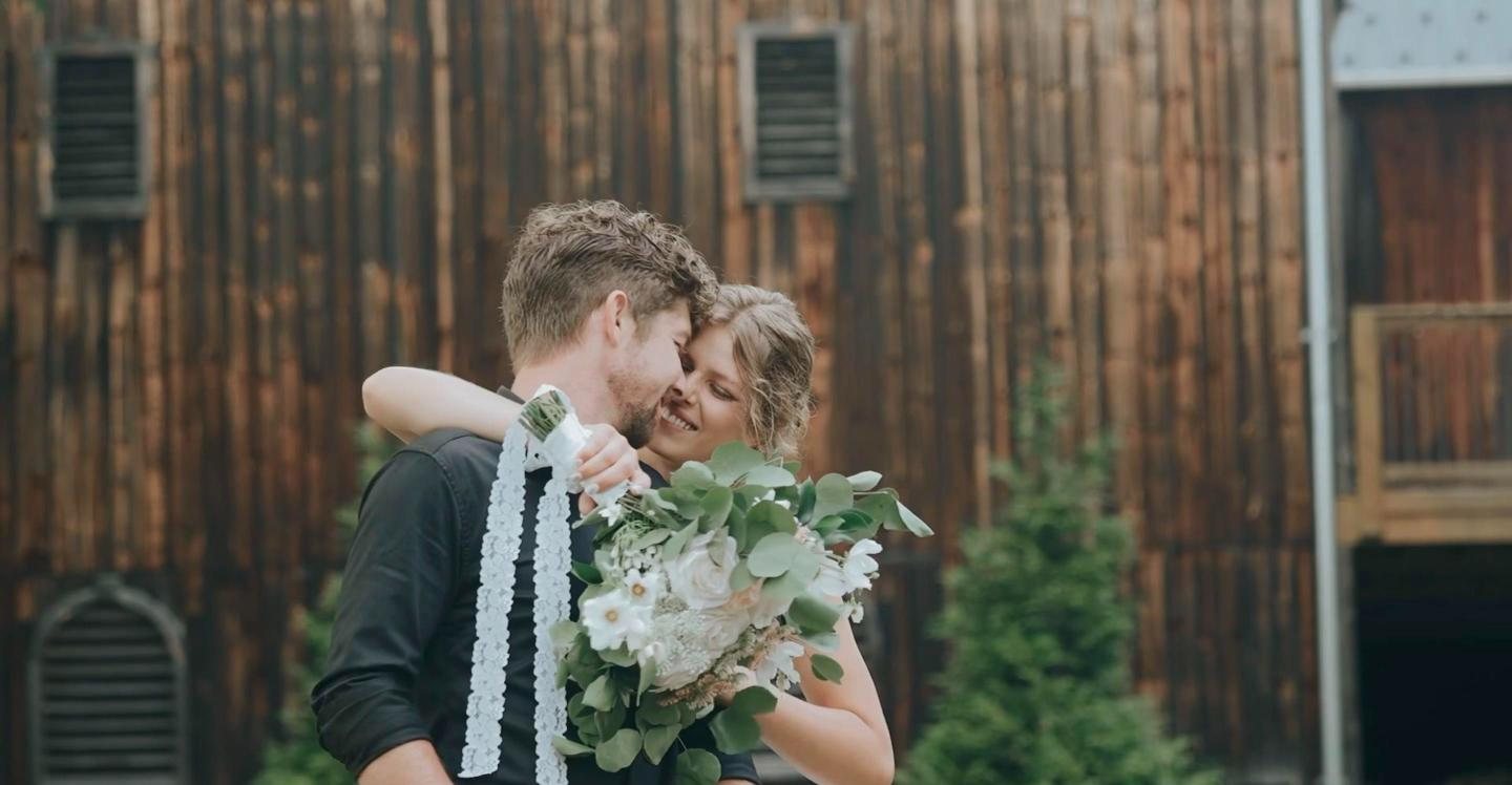 Bride and groom embracing against old barn siding